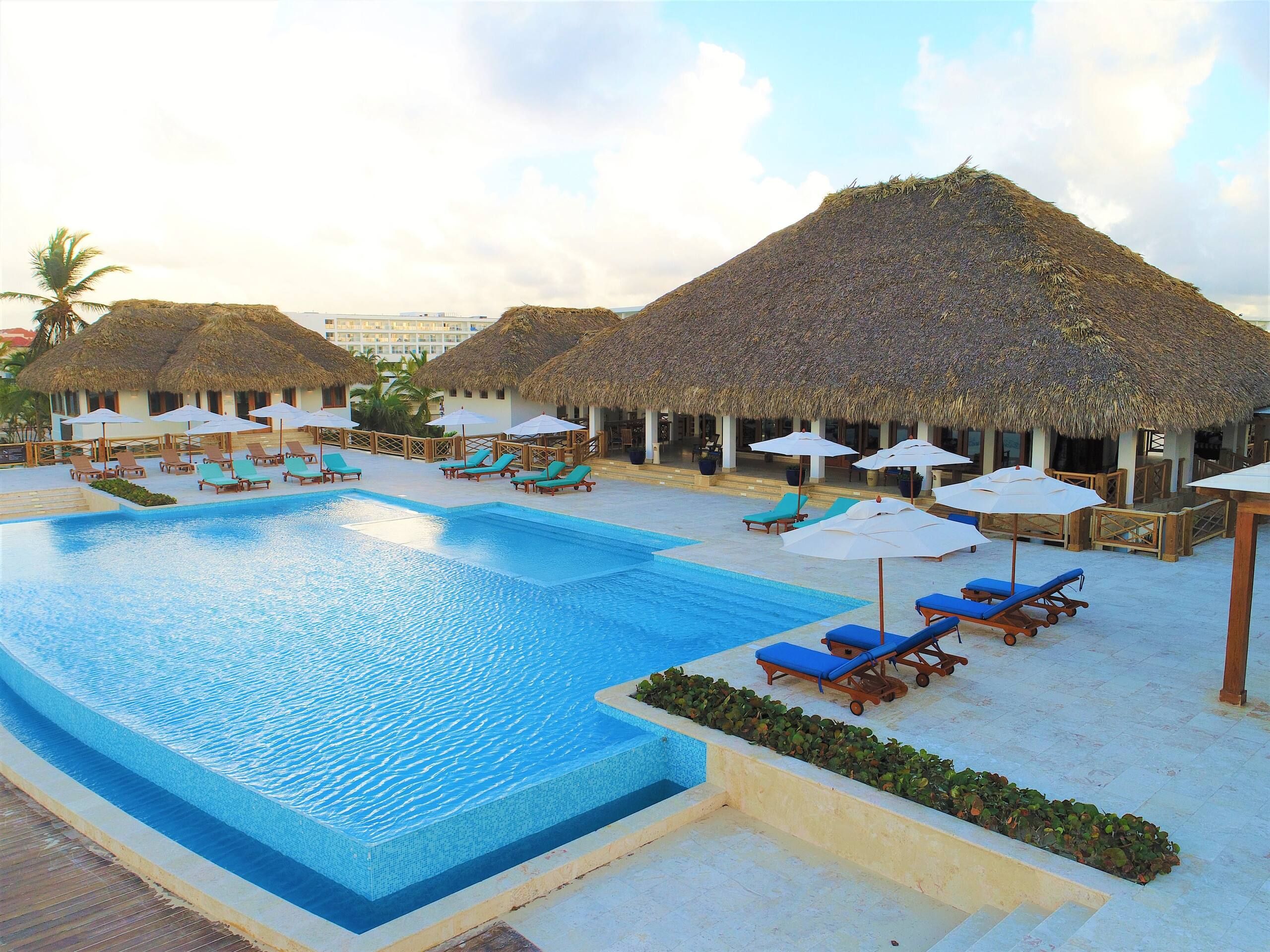 Cana Bay Beach Club pool with thatched palapas, umbrellas and blue loungers